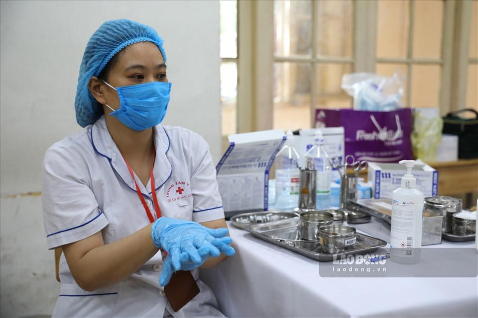 Nhân viên y tế thực hiên sát khuẩn tay/thay gang tay y tế sau khi hoàn thành 1 mũi tiêm cho người dân.