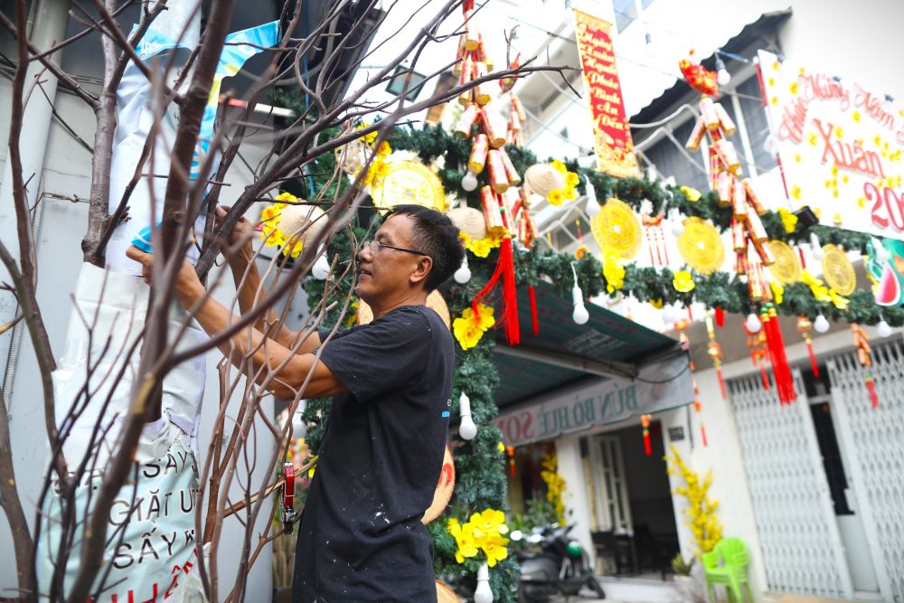 Ông Hoàng Dũng (hẻm 174 Bàn Cờ) cho biết, cứ đến gần Tết, ông cùng vài người hàng xóm trang trí.  “Không có nhiều kinh phí để chưng mai, đào thật, tôi dùng cây khô và các vật liệu đơn giản có sẵn để làm cây mai, gắn hoa giả và đèn nháy, vừa dễ làm mà lại ít tốn kém. Quan trọng là tạo thêm không khí cho bà con trong xóm đón Tết, cảm thấy ấm cúng khi về hẻm nhà mình“, ông Dũng nói.