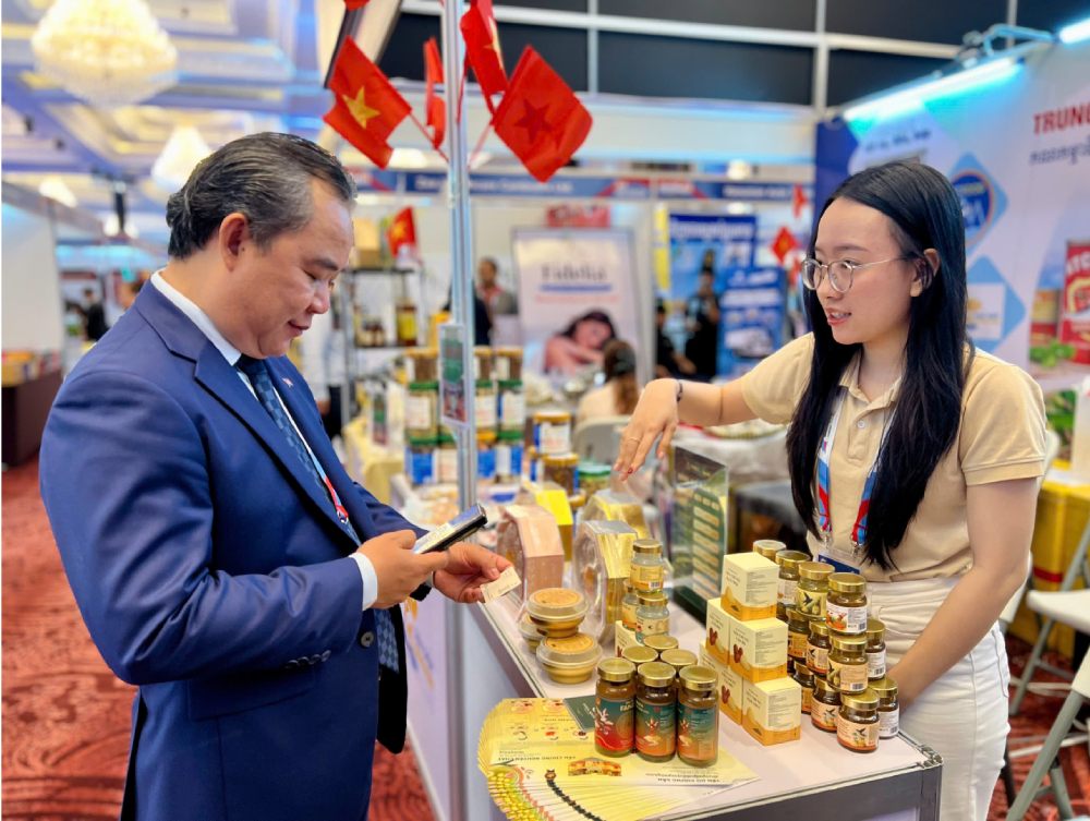 Hướng dẫn cho vị khách người Campuchia quét mã QR để xem thêm thông tin sản phẩm của công ty bằng tiếng Anh. Ảnh: Thiện Thanh