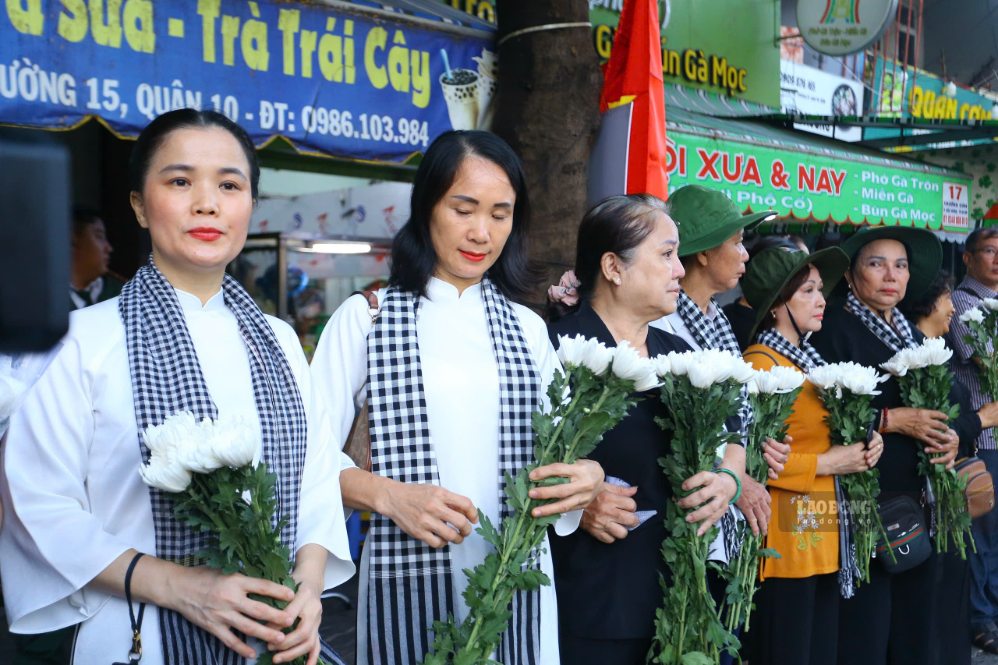 Người dân cầm hoa đứng bên đường, đối diện công viên Lê Thị Riêng để chờ tiễn đưa các liệt sĩ. Ảnh: Thanh Vũ