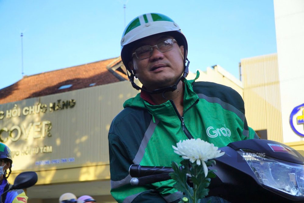 Ông Trần Xuân Phú (ngụ phường Phú Lâm, TPHCM), một tài xế xe công nghệ, đã tạm tắt ứng dụng nhận khách, treo sẵn nhành hoa trắng trên xe. Ảnh: Chân Phúc